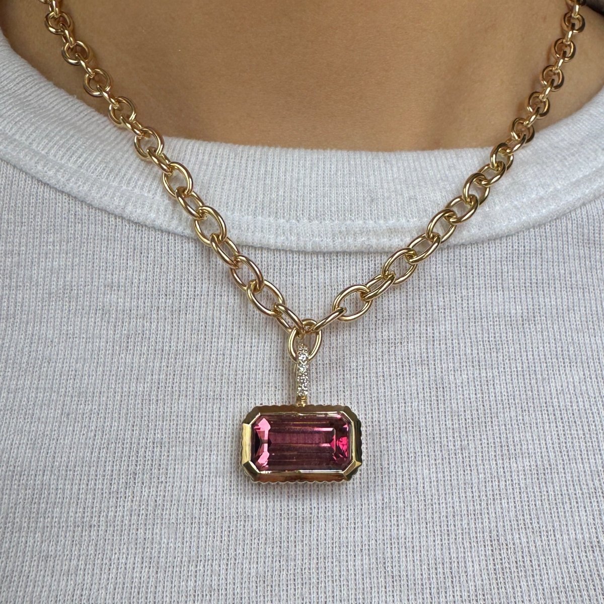 Person wearing a gold pendant with emerald-cut pink tourmaline and a diamond bail on a gold chain against a white shirt