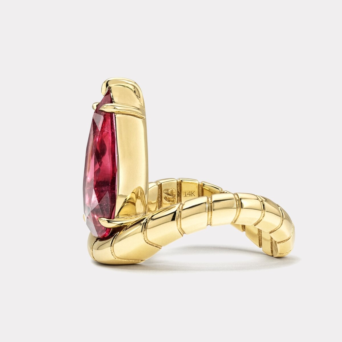 Gold ring with a curved band and a pear shaped pink rubellite against a white background