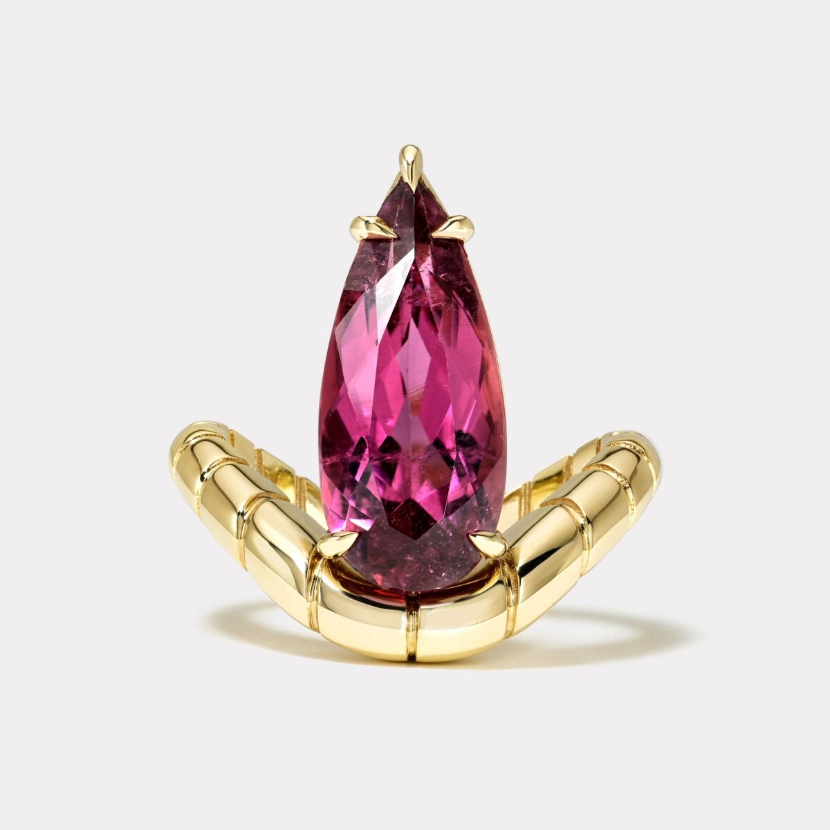 Gold ring with a curved band and a pear shaped pink rubellite against a white background