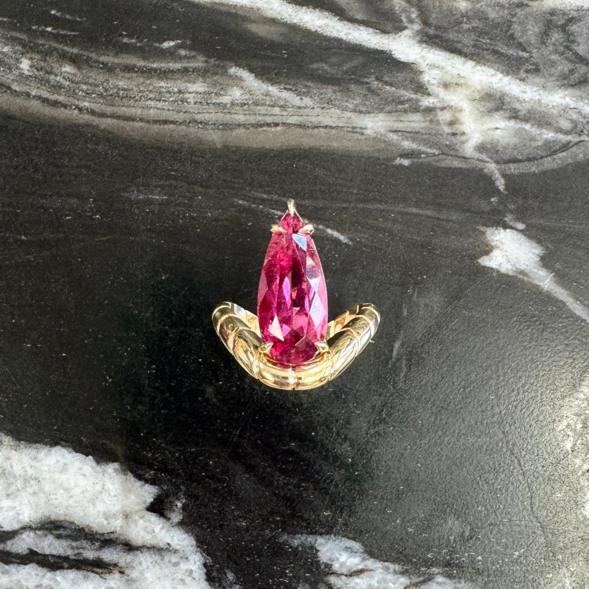 Gold ring with a curved band and a pear-shaped rubellite against a black and white marble background