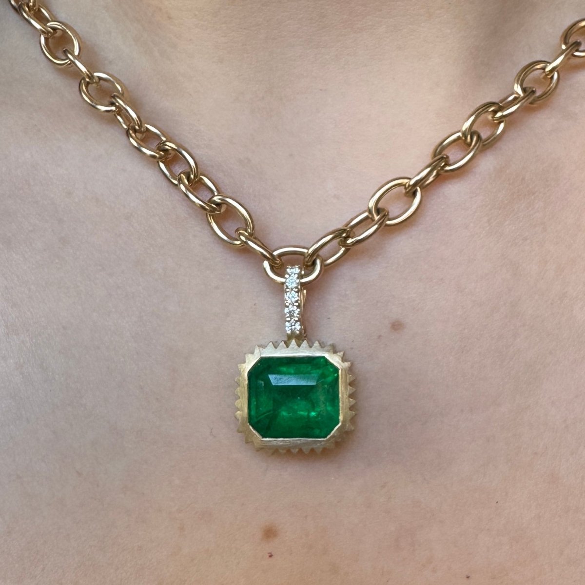 Person wearing a gold pendant with an emerald and a diamond bail on a gold chain