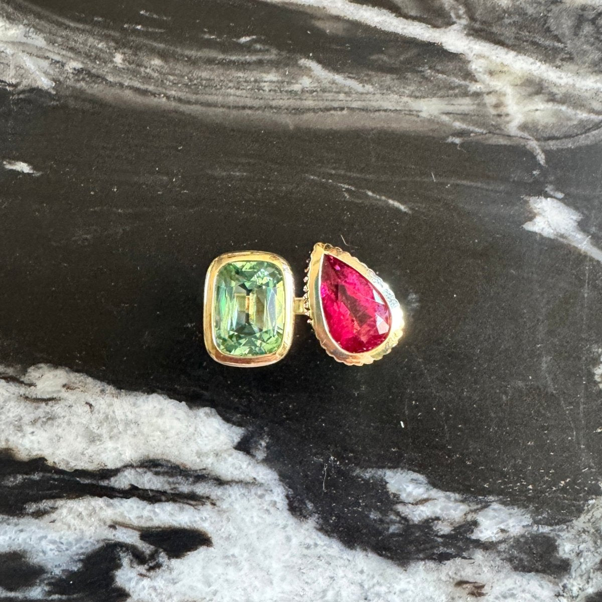 Gold ring with an elongated cushion-cut mint tourmaline and a pear-shaped pink red rubellite against a black and white marble background