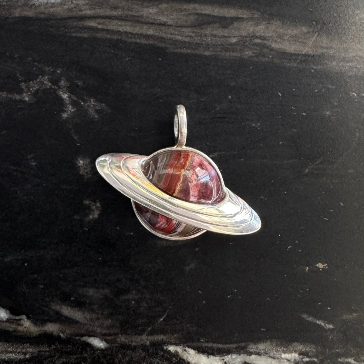 Silver Saturn-shape pendant with red Mexican lace agate against a black and white marble background