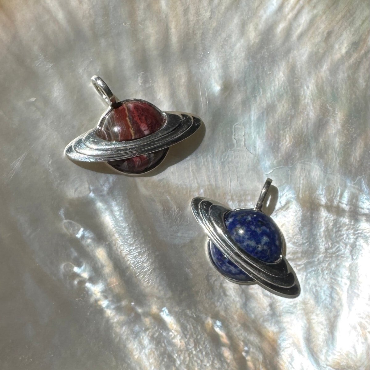 Multiple silver Saturn-shape pendants with multicolored inlay against a pearlescent background 