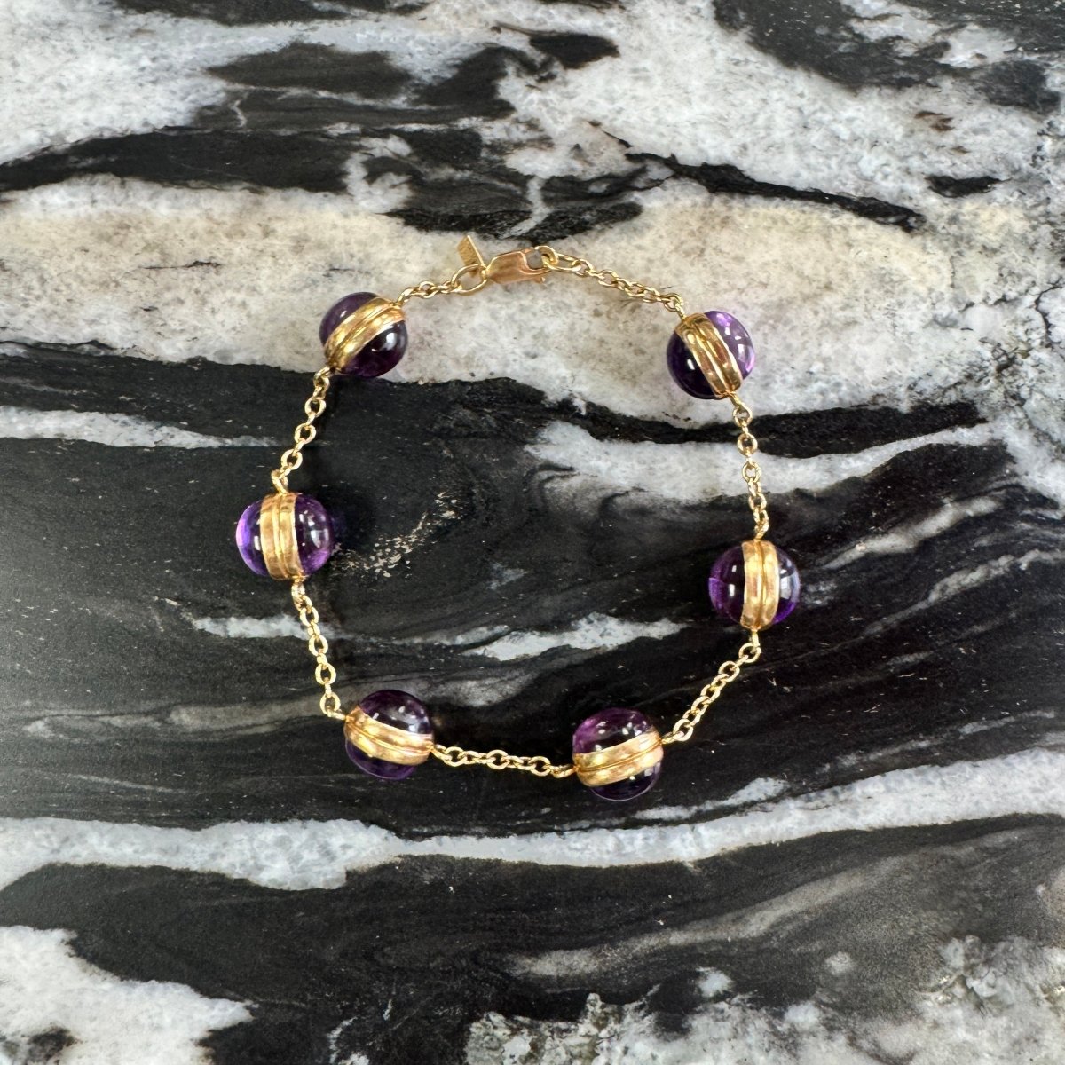 Gold bracelet with purple beads on a marble surface