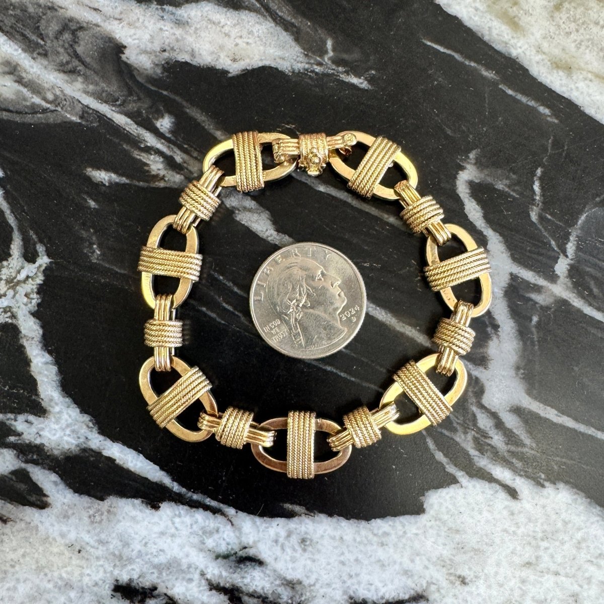 Gold anchor link chain bracelet with rope detailing and a quarter for size reference against a black and white marble background