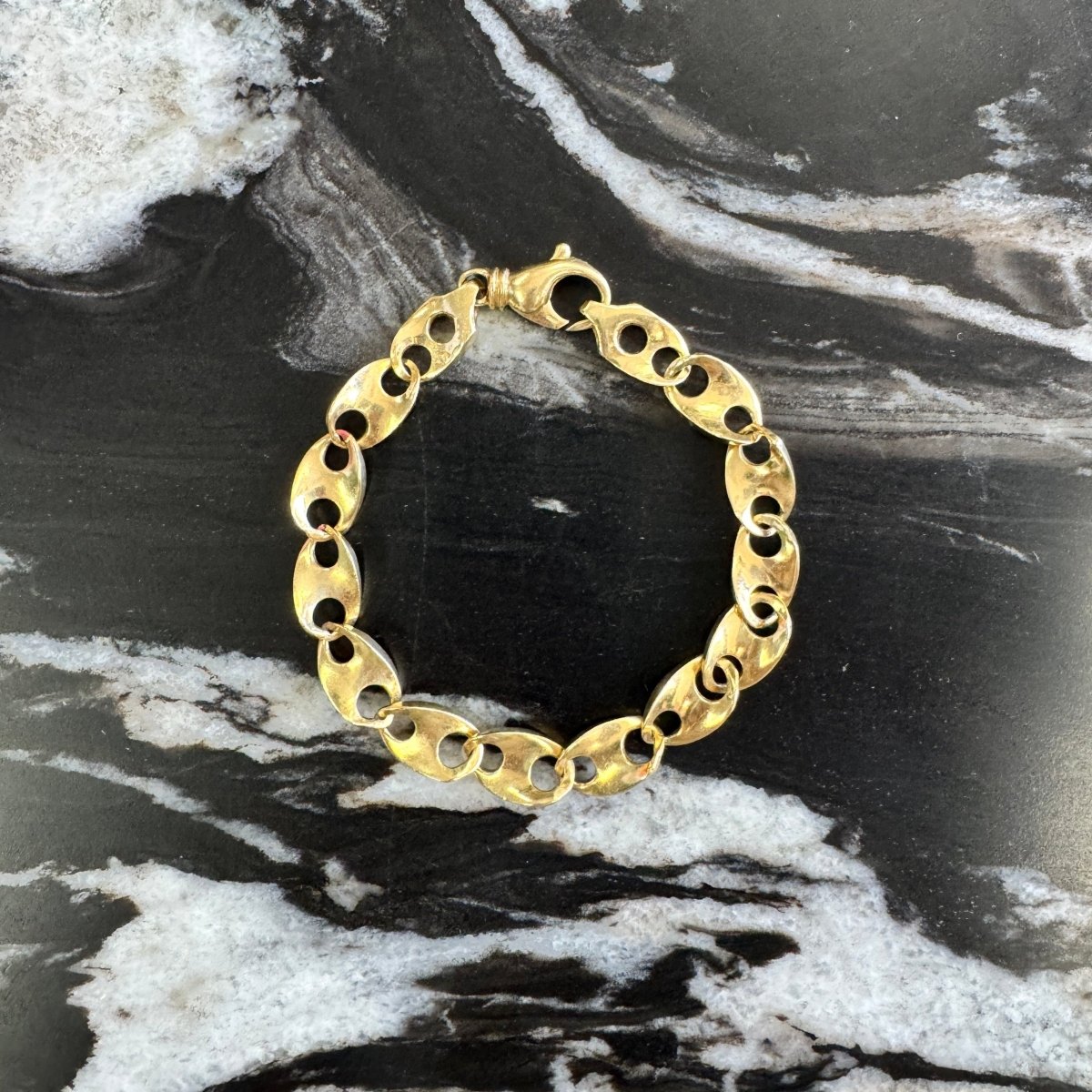 Gold chain bracelet on a black and white marbled surface