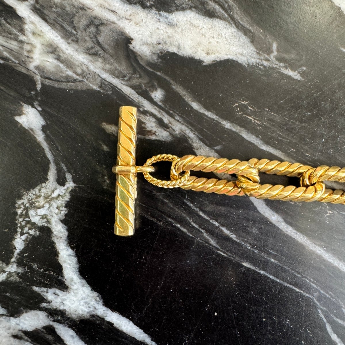 Close up of a gold oval link bracelet with rope texture against a black and white marble background