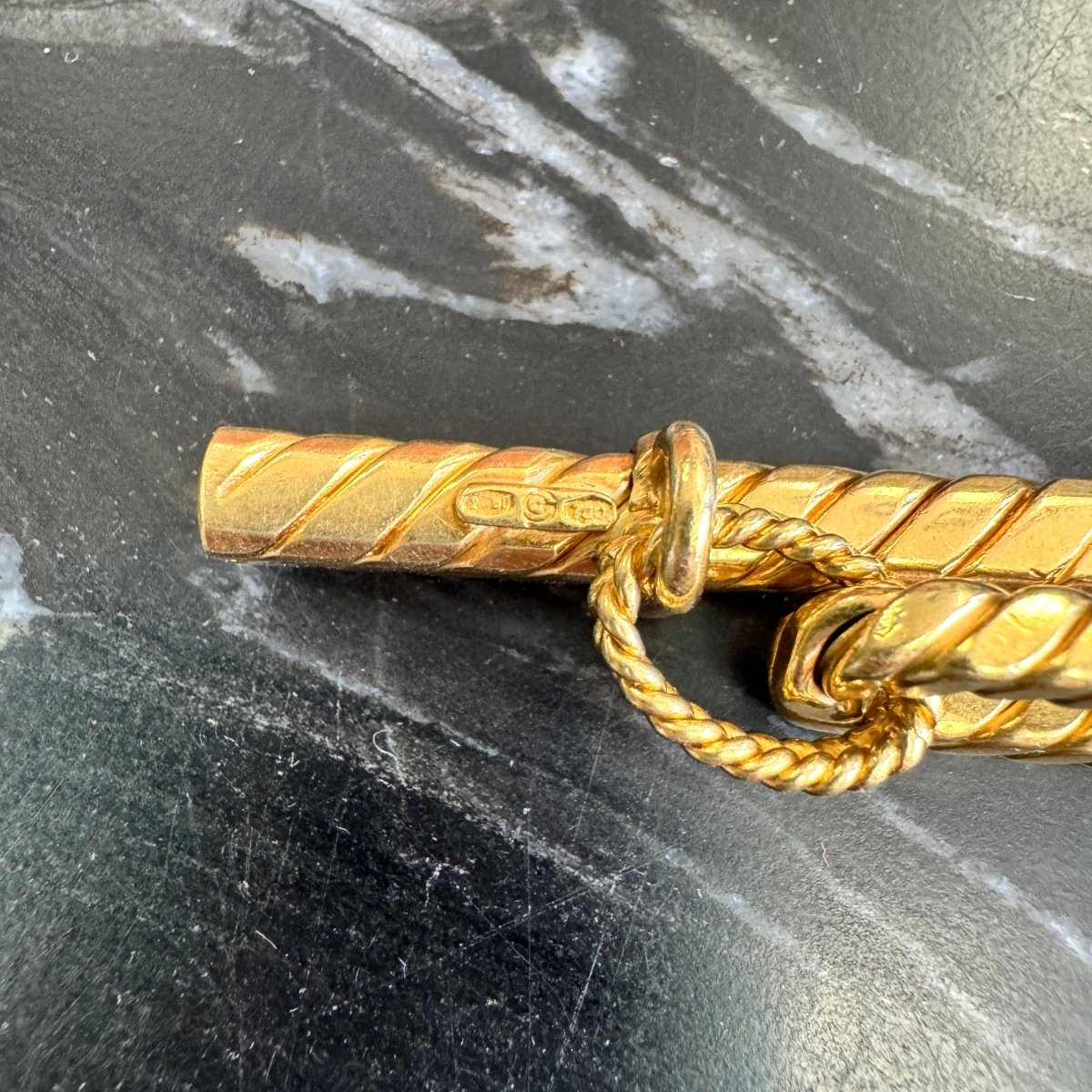 Close up of a makers mark on a gold oval link bracelet with rope texture against a black and white marble background